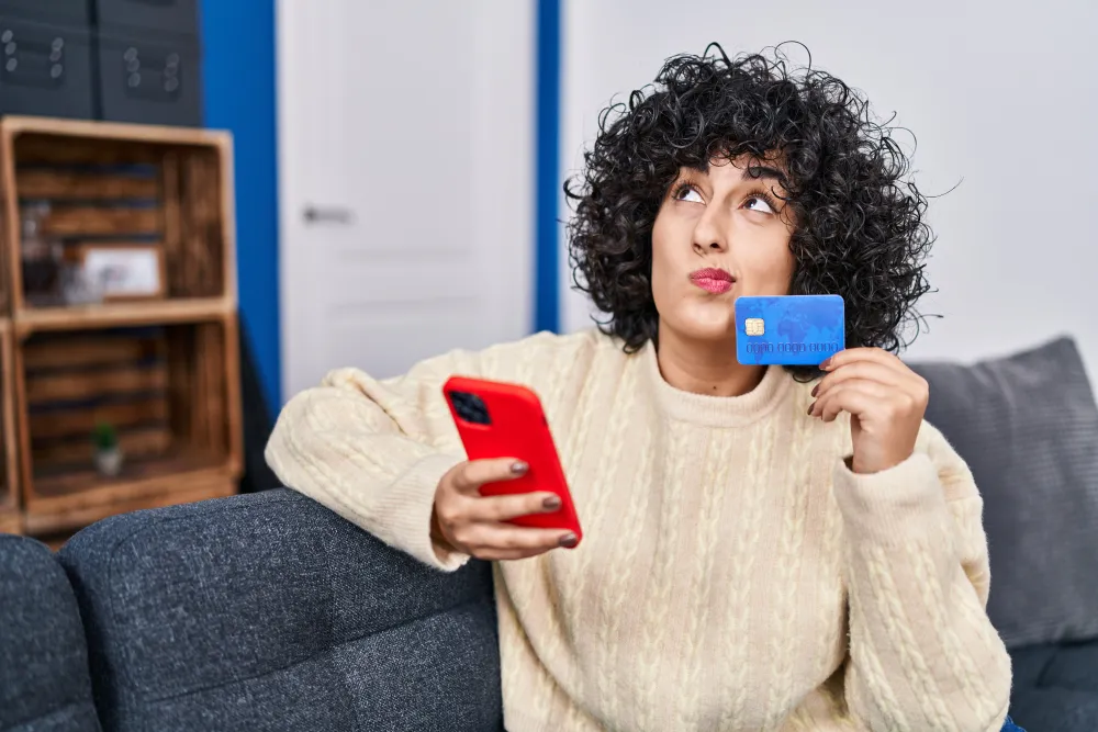 Frau sitzt auf dem Sofa mit Smartphone und Karte in der Hand