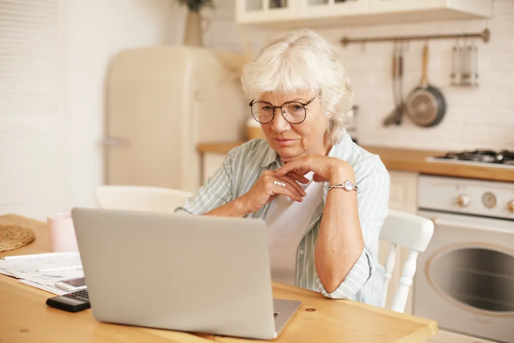 Ältere Frau liest konzentriert Angaben auf ihrem Laptop